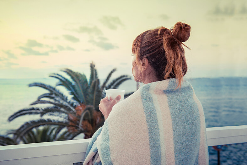 Woman with mug wrapped in Blanket looking at ocean